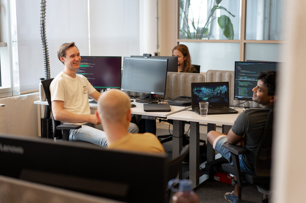 A photo of four developers at the arculus office. They are all talking to each other while working, and appear happy.