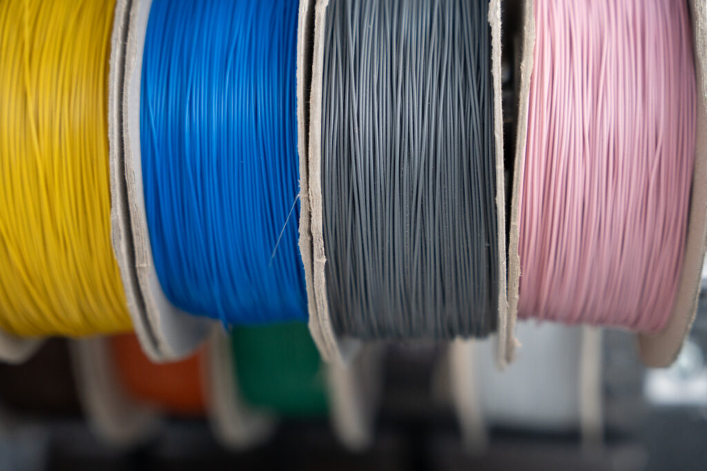 Four cable drums in different colours. From left to right: yellow, blue, dark grey, and pink.